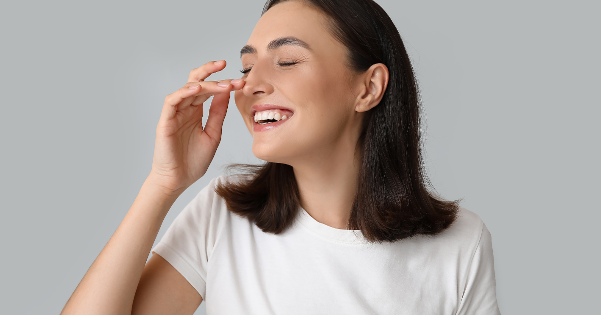 Woman gently touching her nose while smiling, representing confidence and satisfaction after natural revision rhinoplasty results
